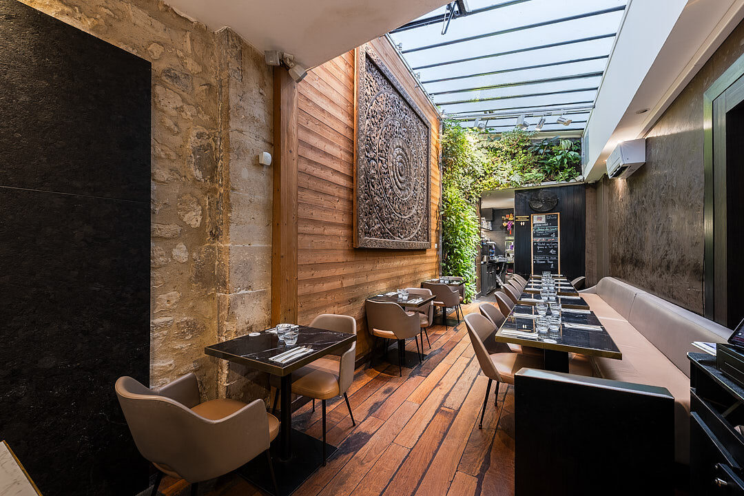 Intérieur du restaurant Suan thai avec tables dressées, décorations, sculpture en bois et murs végétal à Paris dans le Marais.