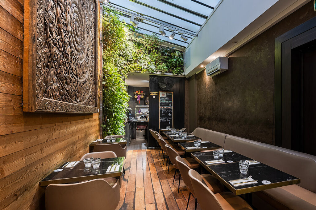 Intérieur du restaurant Suan thai avec tables dressées, décorations, sculpture en bois et murs végétal.