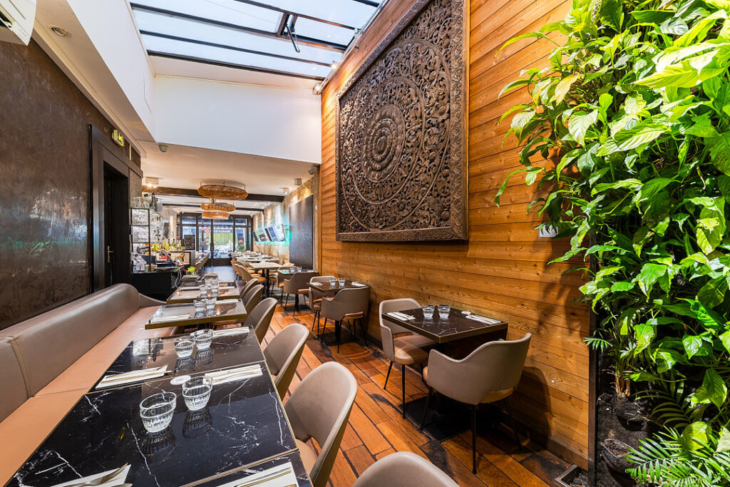 Intérieur du restaurant Suan thai avec tables dressées, décorations, sculpture en bois et murs végétal.