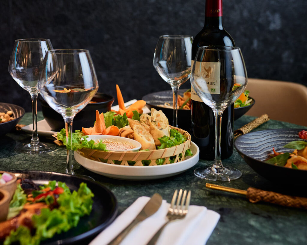 Table en marbre verre dressées de plats thaïlandais et bouteille de vin rouge.