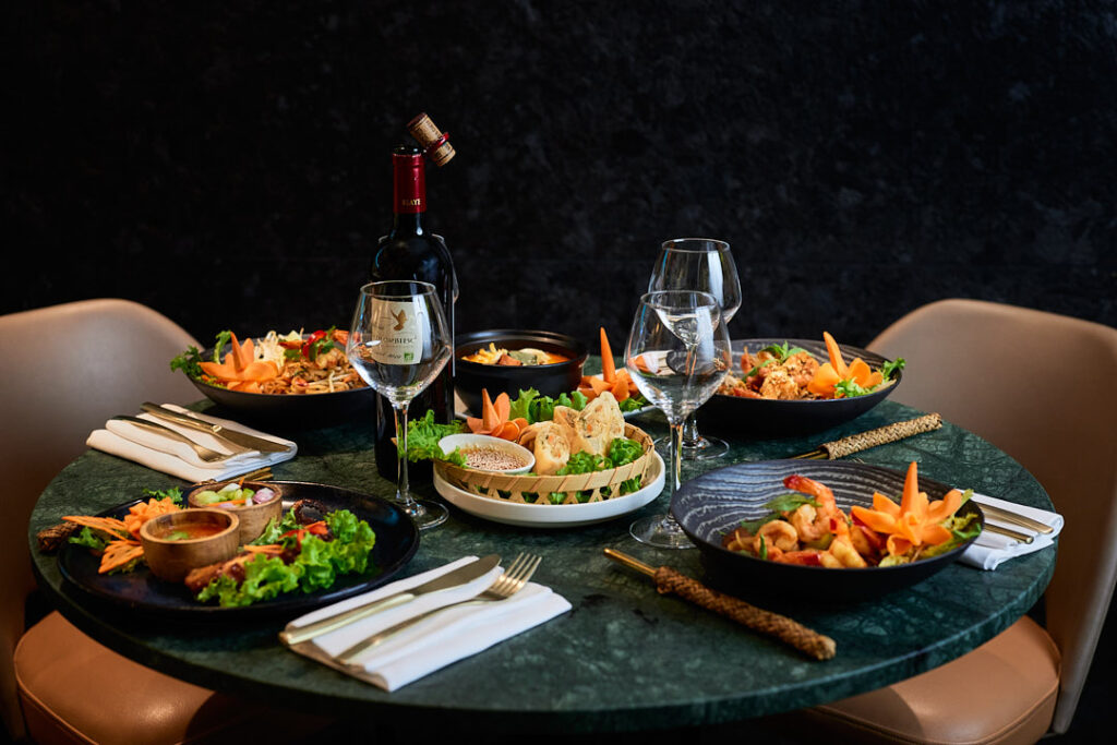 Table en marbre verre dressées de plats thaïlandais et bouteille de vin rouge.