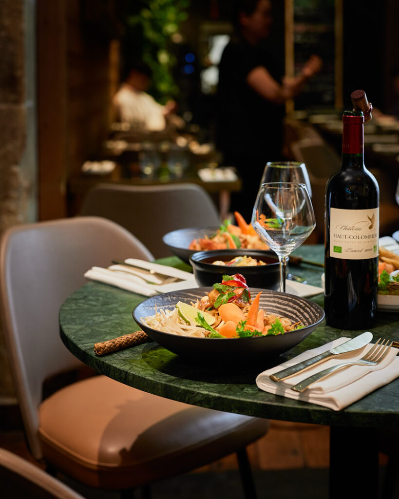 Table en marbre verre dressées de plats thaïlandais et bouteille de vin rouge.