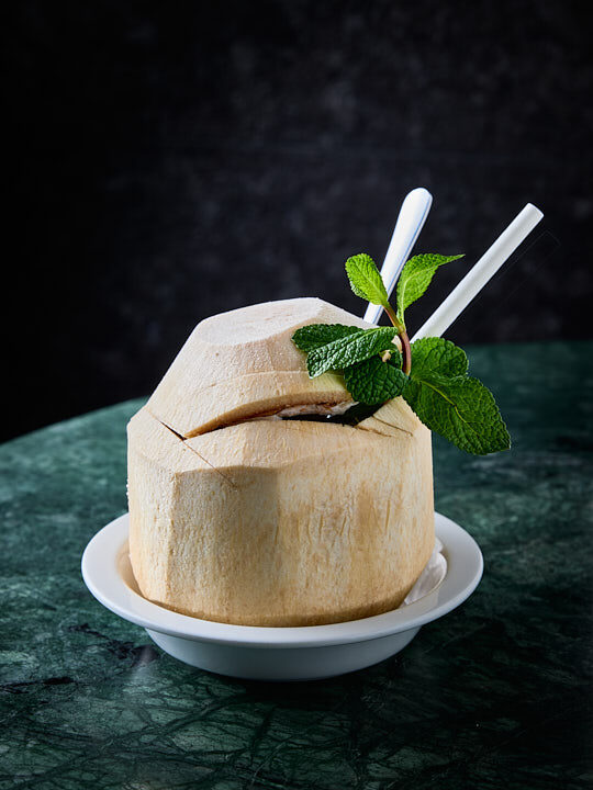 jus de noix de coco servi dans son écorce sur une table en marbre vert